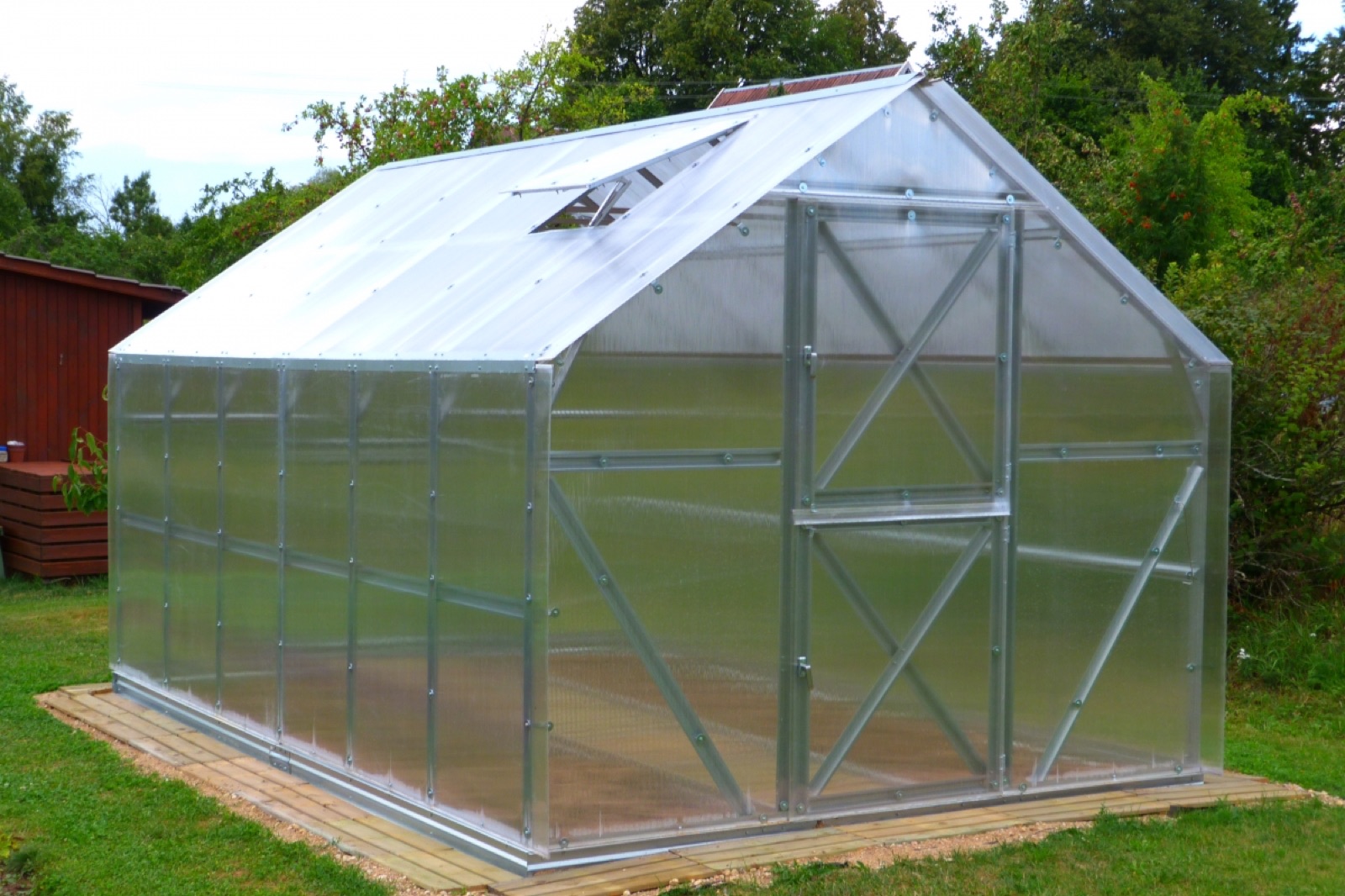A bolted steel-frame polycarbonate greenhouse in a backyard garden